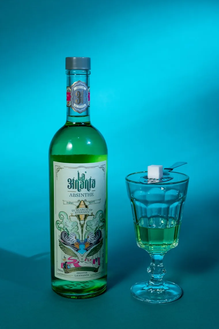 A bottle of La'Ananta Absinthe beside a glass of green absinthe topped with a sugar cube