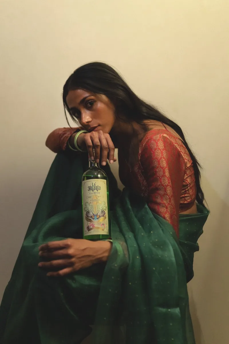 A woman in a green sari seated with a bottle of La'Ananta Absinthe