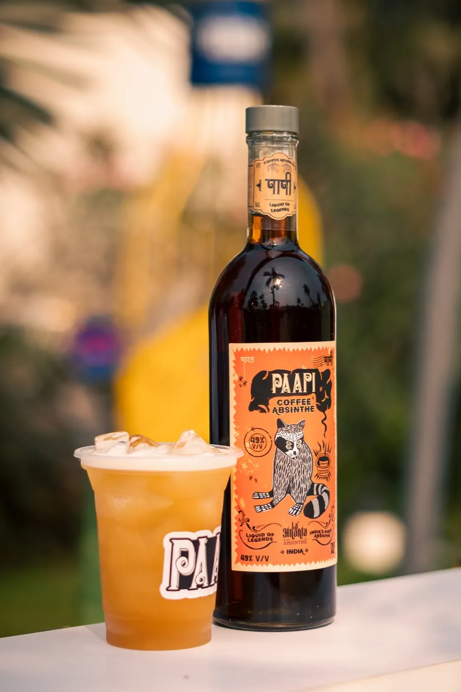 Paapi served long over ice in a branded cup, beside the bottle